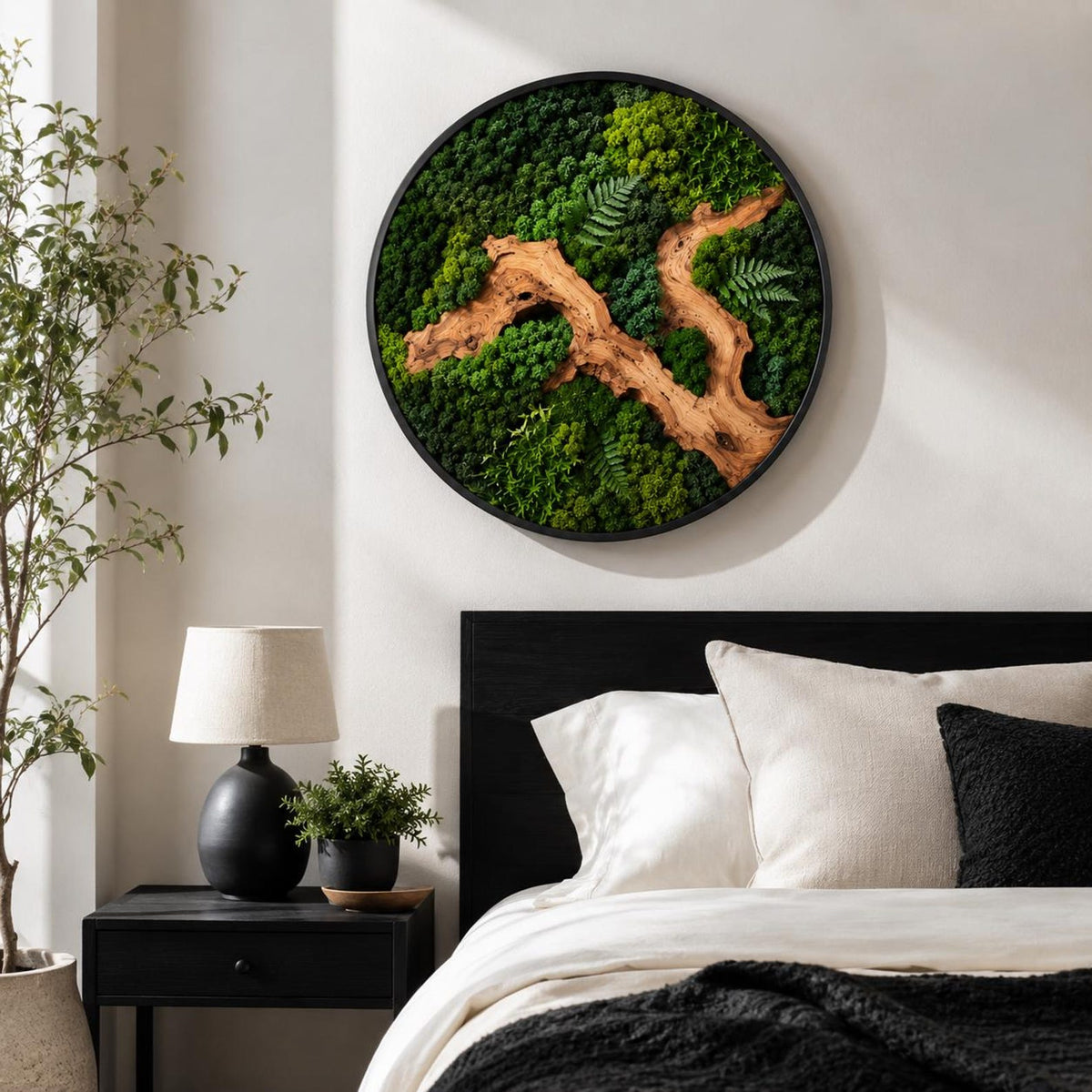 A circular wall art piece featuring a dense arrangement of preserved green moss in various shades, accented by a prominent, winding piece of light brown driftwood and delicate fern fronds, all enclosed within a thin black frame.