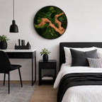 A circular wall art piece featuring a natural wood branch centerpiece surrounded by dense, vibrant green preserved moss and small fern fronds, all encased within a thin, black circular frame mounted on a plain white wall.