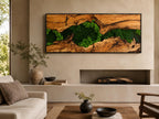 A rectangular wall art piece featuring a natural wood slab with a prominent grain pattern and a central crevice filled with vibrant green preserved moss, all enclosed within a thin black frame mounted horizontally on a wall.