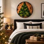 A circular wall art piece featuring a natural wood slice frame with a tree-shaped arrangement of preserved green moss. The artwork is mounted on a wall above a bed with white and black pillows and a dark green chunky knit blanket.