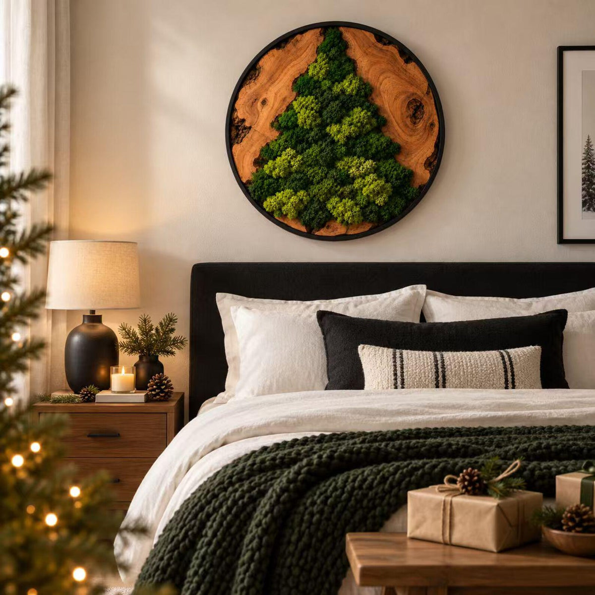 A circular wall art piece featuring a natural wood slice frame with a tree-shaped arrangement of preserved green moss. The artwork is mounted on a wall above a bed with white and black pillows and a dark green chunky knit blanket.