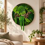 A circular wall art piece featuring preserved green moss in various shades and textures, accented by a piece of natural driftwood. The arrangement is contained within a thin, circular frame, creating a dense, organic display.