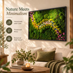 A rectangular wall art piece featuring preserved green moss in various shades and textures, accented by a winding path of small pink, yellow, and white flowers. The artwork is encased in a thin black frame and mounted on a wall.