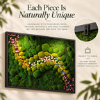 A rectangular wall art piece featuring preserved green moss and small colorful flowers in a black frame. Text reads: Each Piece Is Naturally Unique, Handmade with preserved moss, natural materials and real flowers. No two designs are ever the same. Ready to hang includes secure hanging hardware for easy installation.