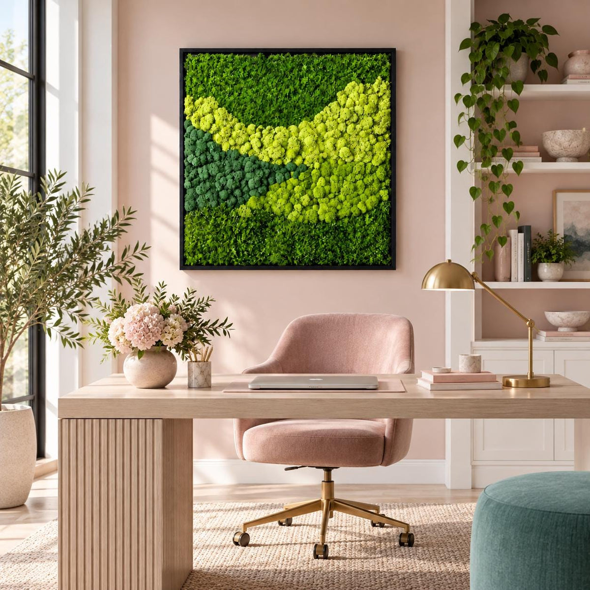 A square wall art piece featuring a dense arrangement of preserved moss in varying shades of vibrant lime green and deep forest green, encased in a thin black frame, mounted on a light pink wall above a wooden desk and chair.