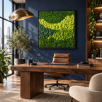 A square wall art piece featuring a dense arrangement of preserved moss in varying shades of vibrant lime green, forest green, and deep emerald green, encased in a thin black frame and mounted on a dark navy blue wall.