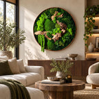 A circular wall art piece featuring a dense arrangement of vibrant green preserved moss and natural driftwood branches. The composition is contained within a thin, circular frame, showcasing various textures of moss and wood.
