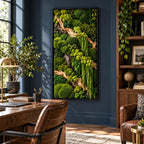 A rectangular wall art piece featuring a dense arrangement of preserved green moss in various textures and shades, accented by light-colored driftwood branches, all enclosed within a thin, black frame mounted on a dark blue wall.