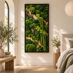 A rectangular wall art piece featuring a dense arrangement of preserved green moss in various shades and textures, accented by light-colored driftwood branches, all enclosed within a thin, black frame mounted on a neutral wall.