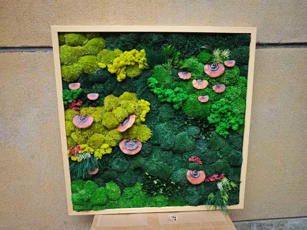 A square wall art piece featuring a light wood frame filled with preserved moss in various shades of lime, forest, and emerald green. The arrangement includes several small, reddish-brown, circular shelf fungi attached to the moss.