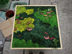 A square wall art piece featuring a preserved moss arrangement in a light wood frame. The composition includes various shades of green moss, small red accents, and several brown, shelf-like fungi distributed across the surface.