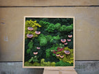 A square wall art piece featuring a wooden frame filled with preserved moss in various shades of green, ranging from lime to dark forest tones. Several brown, shelf-like fungi are attached throughout the textured moss arrangement.