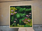 A square wall art piece featuring a dense arrangement of preserved green moss in various shades, including lime and dark forest green. The composition is accented with several small, circular, reddish-brown shelf fungi.