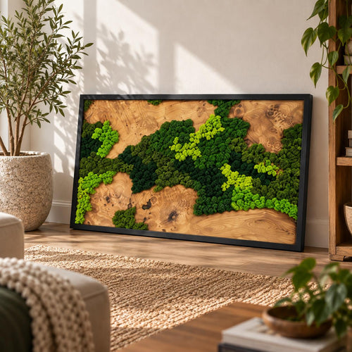 A rectangular wall art piece featuring a natural wood grain background with a black frame. The surface is decorated with preserved moss in various shades of bright lime green, forest green, and dark emerald green textures.
