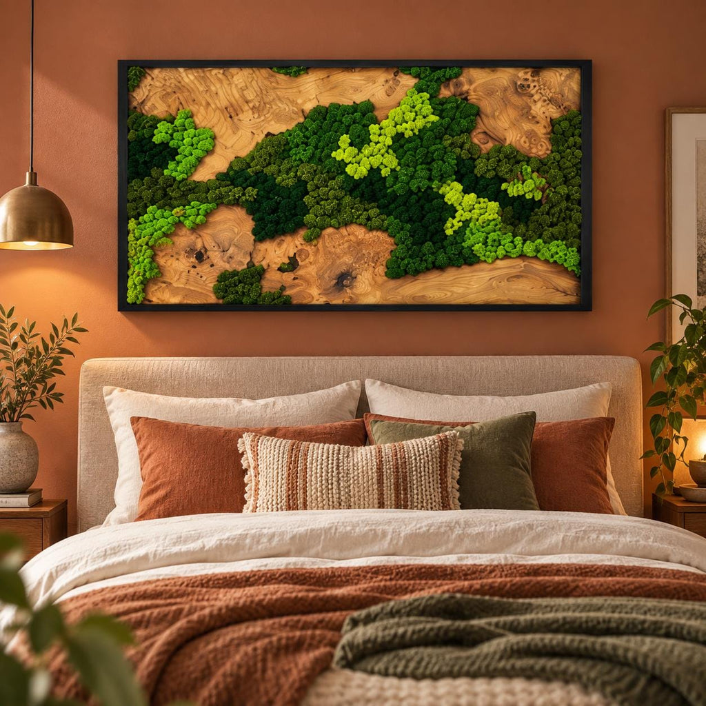 A rectangular wall art piece featuring a natural wood slab background with clusters of preserved green moss in varying shades of lime and forest green, all enclosed within a thin black frame mounted above a bed.