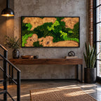 A rectangular wall art piece featuring a natural wood slab with organic grain patterns and patches of preserved bright lime and dark forest green moss, enclosed in a thin black frame and mounted on a gray concrete wall.