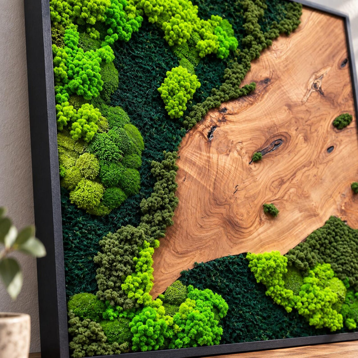 A square wall art piece featuring a black frame containing a natural wood slab with a prominent grain pattern, accented by clusters of preserved moss in varying shades of bright lime green, forest green, and deep dark green textures.