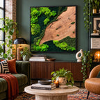 A square wall art piece featuring a natural wood slab section contrasted with vibrant green preserved moss in various textures and shades, all encased within a thin black frame, mounted on a dark green wall above a wooden sideboard.