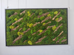 A rectangular wall art piece framed in black, featuring a dense arrangement of preserved moss in various shades of forest and lime green, interspersed with diagonal strips of textured brown tree bark across the surface.