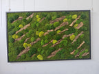 A rectangular wall art piece featuring a dense arrangement of preserved green moss in various shades, including bright lime and deep forest green, interspersed with diagonal strips of textured brown tree bark inside a black frame.