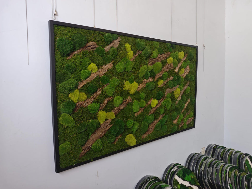 A rectangular wall art piece featuring a black frame filled with preserved green moss in various shades of lime and forest green, interspersed with diagonal strips of textured brown tree bark arranged in a repeating pattern.