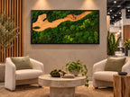 A rectangular wall art piece featuring a natural wood grain section flowing through dense, preserved green moss, all encased in a thin black frame. The composition mimics a river landscape with varied textures of vibrant green moss.