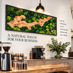 A rectangular wall art piece featuring preserved green moss and a central winding wood grain pattern in a black frame. The wall displays the text A NATURAL TOUCH FOR YOUR BUSINESS and a list of coffee drinks including COFFEE, ESPRESSO, LATTE.