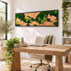 A rectangular wall art piece featuring a natural wood grain background accented with patches of preserved dark green and bright lime green moss, all enclosed within a thin black frame mounted on a white wall above a wooden desk.