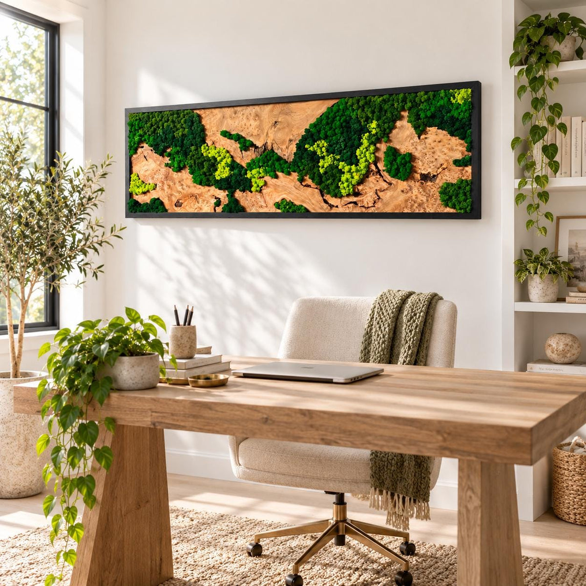 A rectangular wall art piece featuring a natural wood grain background accented with patches of preserved dark green and bright lime green moss, all enclosed within a thin black frame mounted on a white wall above a wooden desk.